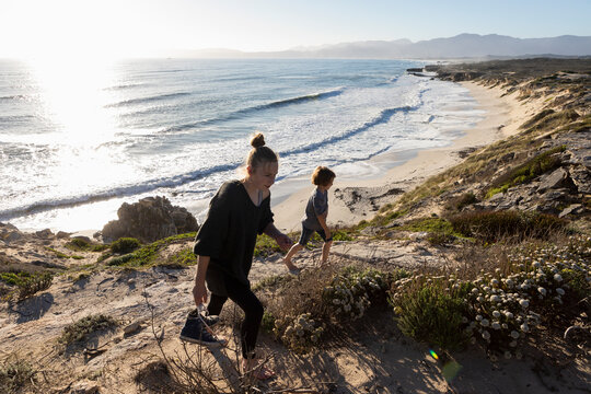 A teenage girl and her brother running down a path towards a sandy beach