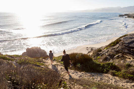 A teenage girl and her brother running down a path towards a sandy beach