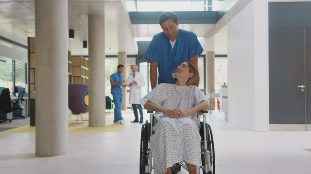 Male nurse wearing scrubs pushing female patient in wheelchair through hospital building - shot in slow motion