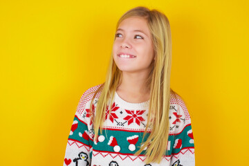 Amazed caucasian little kid girl wearing knitted sweater christmas over yellow background bitting...