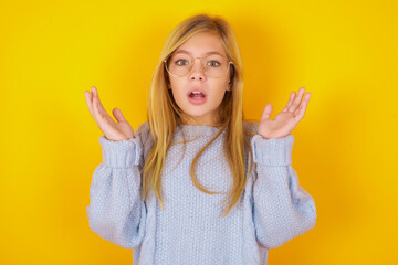 Surprised terrified caucasian kid girl wearing blue knitted sweatGestures with uncertainty, stares at camera, puzzled as doesn't know answer on tricky question, People, body language, emotions concept