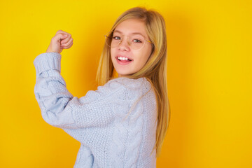 Portrait of powerful cheerful caucasian kid girl wearing blue knitted sweater over yellow...