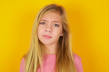Displeased caucasian little kid girl wearing long sleeve shirt over yellow background frowns face feels unhappy has some problems. Negative emotions and feelings concept