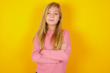Fototapeta premium Confident caucasian little kid girl wearing long sleeve shirt over yellow background with arms crossed looking to the camera