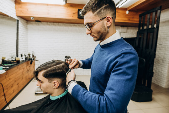 Professional barber fixes clients hair at barbershop with comb side photo