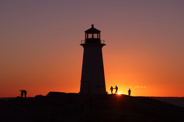 Silhouette shot of a couple and the  lighthouse on a beautiful sunset full of red and orange sky. 
Peggy's Cove Lighthouse, Halifax, Nova Scotia, Canada