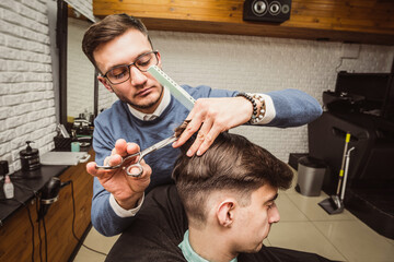 Professional barber trims clients hair with scissors at barbershop side photo