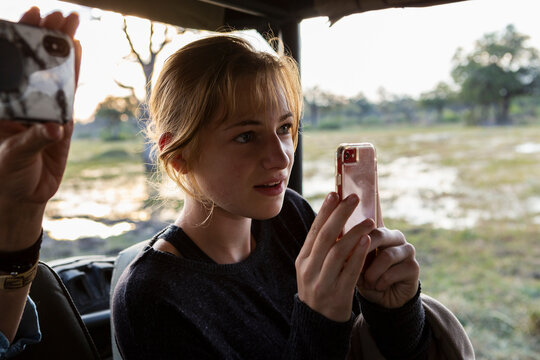 Teenage girl using smart phone to take a picture during a safari jeep drive. 