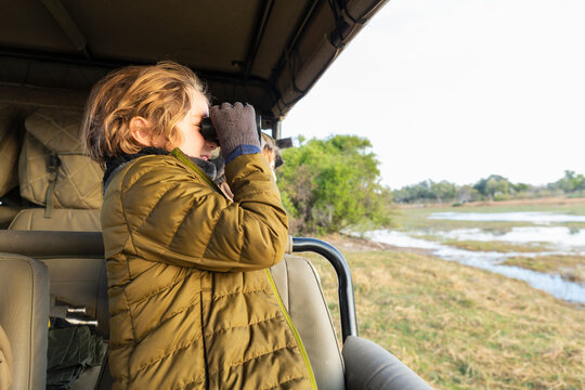 Young boy using binoculars standing in a safari jeep. 