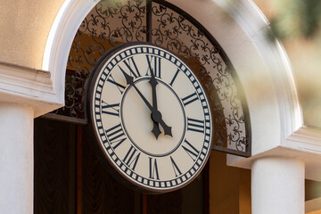 The hands of the clock 7 minutes to 12 on the large white dial of the outer clock on the yellow wall