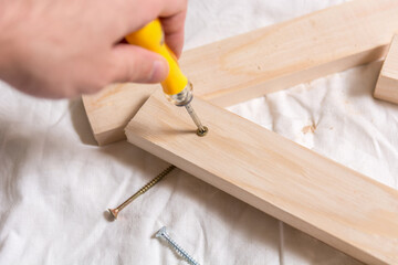 Hand with screwdriver screw bolt in wooden plank in carpenters workshop. Close up, selective focus, and copy space