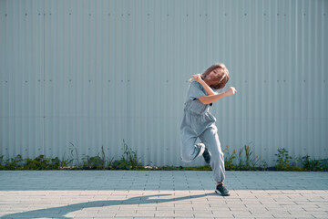 Dancing child girl happy moving on textured street fence background. Energetic cool teen female dancer having fun
