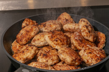 Fry pan full of hot patties on induction hob. White steam hovers over hot cutlets in a frying pan