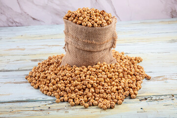 Roasted chickpea. Roasted spicy chickpeas in a straw sack  on wooden white background.