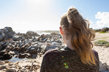 Teenage girl looking out over a beach and jagged rocks to the ocean
