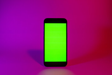 Mobile phone with green screen, smartphone mock up. Neon illumination. Pink and purple color. Flat screen modern smartphone