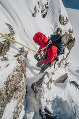 Climber rappeling down an alpine peak. Winter mountaineering, alpinism in Mont Blanc Masiff, France. An alpinist descending on a rope from a mountain.