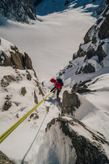 Climber rappeling down an alpine peak. Winter mountaineering, alpinism in Mont Blanc Masiff, France. An alpinist descending on a rope from a mountain.