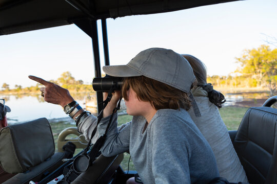 Boy in a safari jeep looking through binoculars.