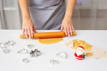 Women's hands are rolling out the dough for Christmas cookies, on a white table