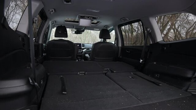 Very large trunk of a modern SUV. all the chairs are folded. black car interior. Panning right