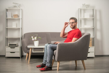 serious guy in red tshirt and eyeglasses work on pc in chair, home office