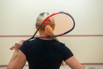 blonde girl stands with her back and holds a racket for squash games