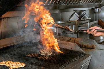 Flames of fire burst as the restaurant kitchen chef flips the cooking hamburger over on the grill