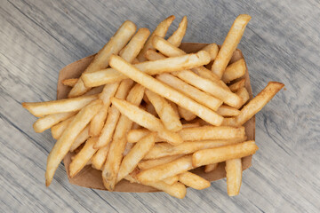 Overhead view of crispy side dish of salty french fries served in a cardboard boat to eat on the go