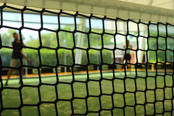 Close up of padel net with two players on the background