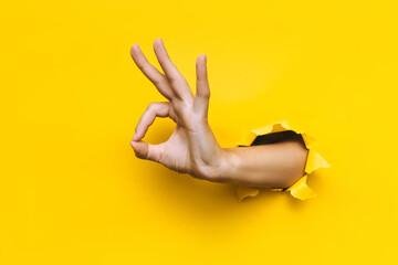 The woman's hand shows with a gesture that everything is fine (ok). Torn hole in yellow paper. The...