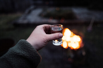 Draußen am Lagerfeuer Schnaps trinken. Mann hält Schnapsglas vor einem Feuer