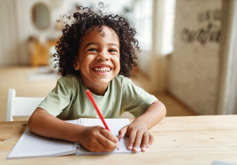 Smiling african american child school boy doing homework while sitting at desk at home - 469809629