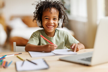Smiling african american child school boy in headphones studying online on laptop at home