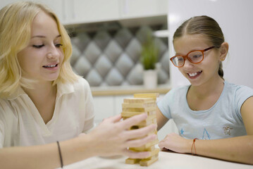 two girls have fun playing Jenga together - board game to remove wooden blocks and kids leisure concept