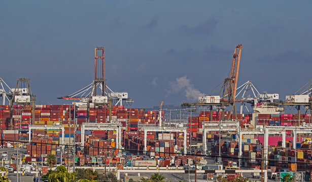 Los Angeles, California USA - November 16, 2021: Gantry cranes tower above container ships in the Port of Los Angeles, while large machines move freight.