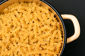 Uncooked Fusilli Pasta in Metal Pot on Black Background. Raw and Dry Macaroni. Unhealthy and Fat Food. Italian Culture
