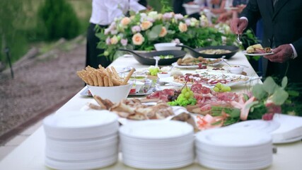 Rich banquet table prepared for exclusive restaurant guests of official exit party, beautifully decorated table with fresh flowers bouquets and assortment of tasty food. Plates with meat slices