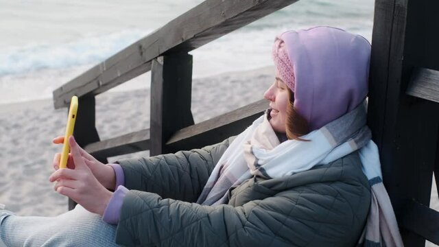 Woman blogger in warm clothes does selphie on the winter beach. Traveller at the cold sea in the off-season