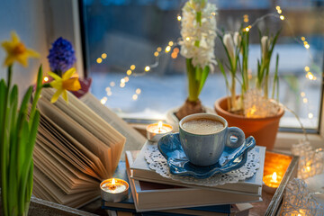 Coffee cup, open book, beautiful flowers, sparkle candles on window with bokeh. Reading and cup of coffee. Concept hygge warm and cozy home interior