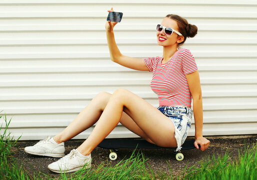 Summer portrait of smiling young woman taking a selfie by smartphone with skateboard on a white background