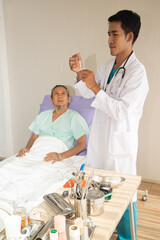 Fototapeta na wymiar Asian male doctor vaccinating arm of Asian elderly male patient in hospital bed.