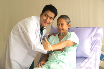 Happy Asian male patient lies on the bed, and raises her thumb up. When a doctor uses a stethoscope to listen to the lungs. Concept of believe in treatment..