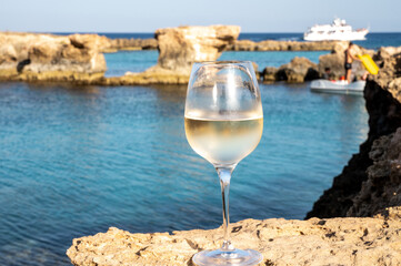 Glass of cold white dry white wine served on rocks in blue sea bay near Protaras touristic town on Cyprus