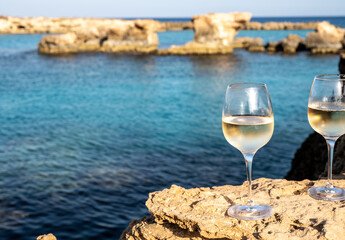 Two glasses of cold white dry white wine served on rocks in blue sea bay near Protaras touristic town on Cyprus