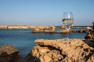 Glass of cold white dry white wine served on rocks in blue sea bay near Protaras touristic town on Cyprus