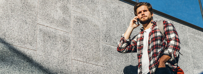 Portrait of modern young man speaking on phone. Hipster guy with mobile in his hand outdoors. Urban...