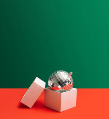 Festive inspired concept. Open gift disposable white box. Shiny disco ball inside it. Creative copy space with green and red background