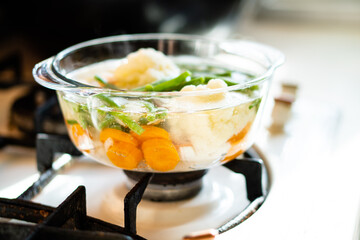 Transparent glass pan with vegetable soup, fresh hot food boils on the stove