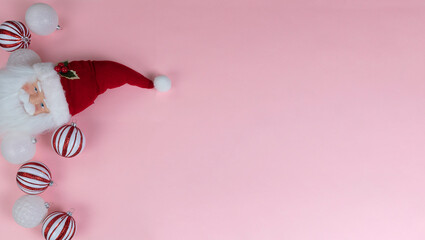 Christmas holiday ball ornaments plus Santa Claus decoration on light pink background in overhead view